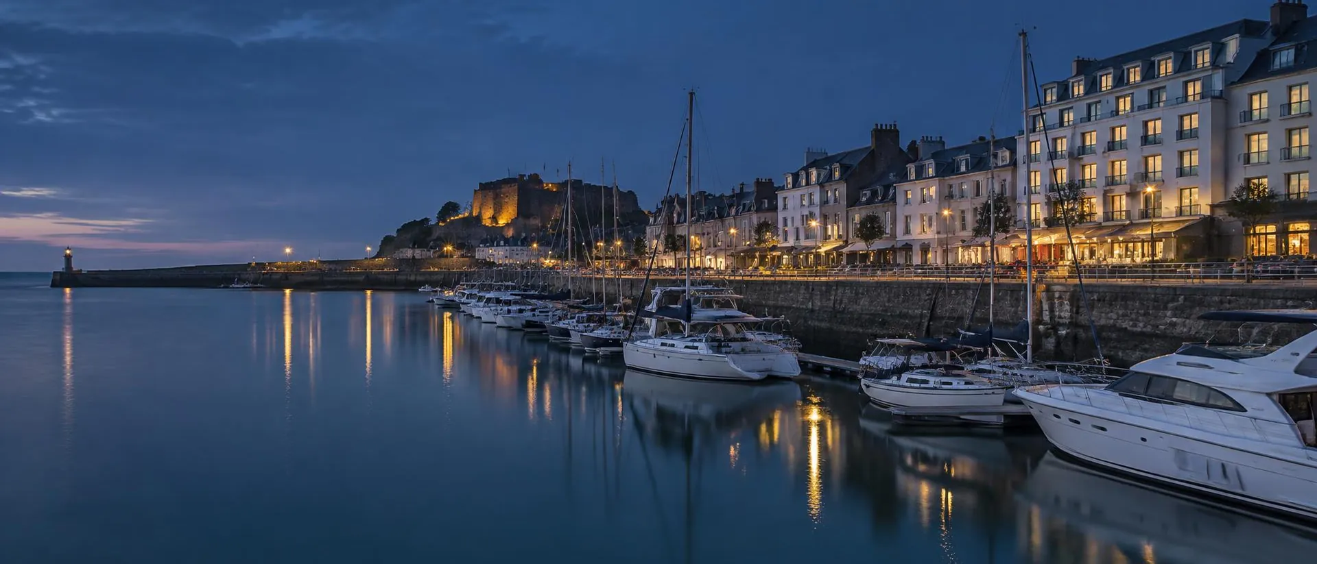 Moored yachts and waterfront lights at St Helier blue hour.